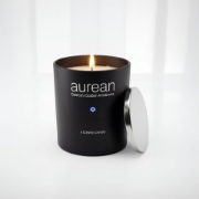 Close-up of Aurean Nox Luxury Candle in a matte black jar with a silver lid and the Greek evil eye emblem, illuminated by a warm flame.