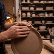 Close-up of an artisan's hands shaping a raw clay plate in a professional pottery studio.